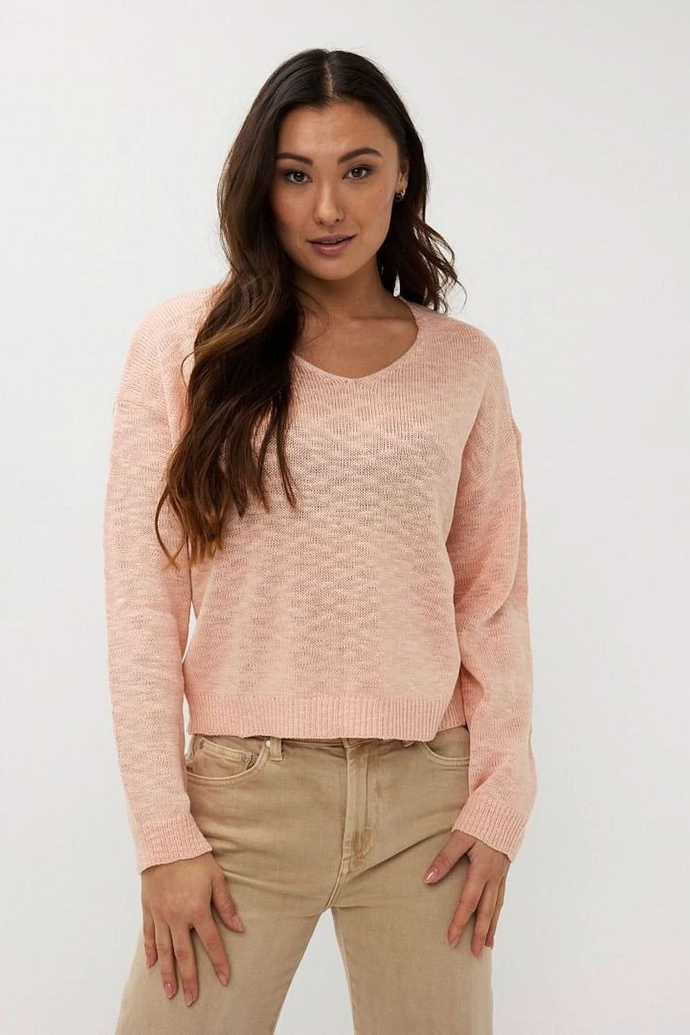 Chandail en tricot ajouré rose avec col en V, manches longues, coupe ample, associé à un pantalon beige.