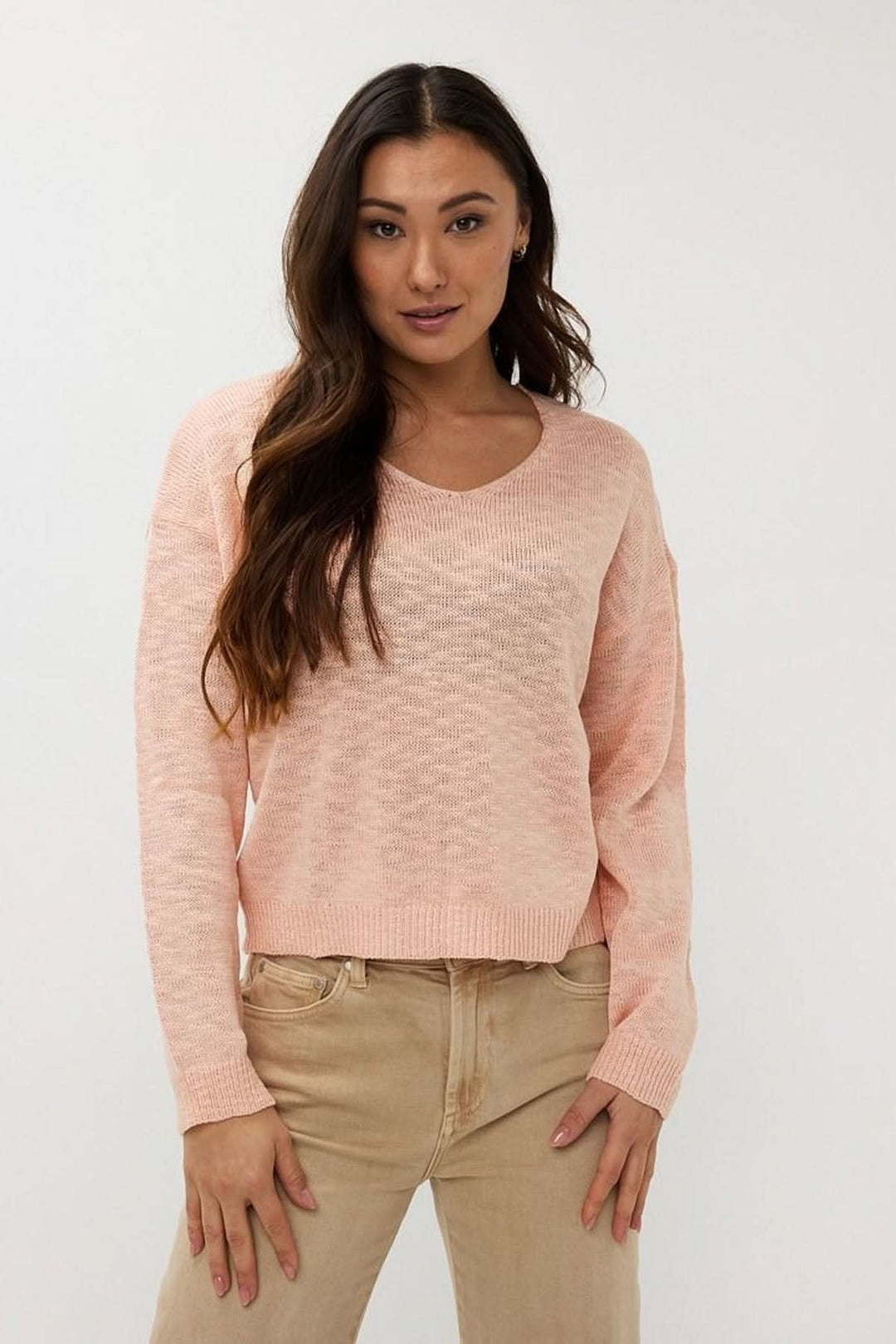 Chandail en tricot ajouré rose avec col en V, manches longues, coupe ample, associé à un pantalon beige.