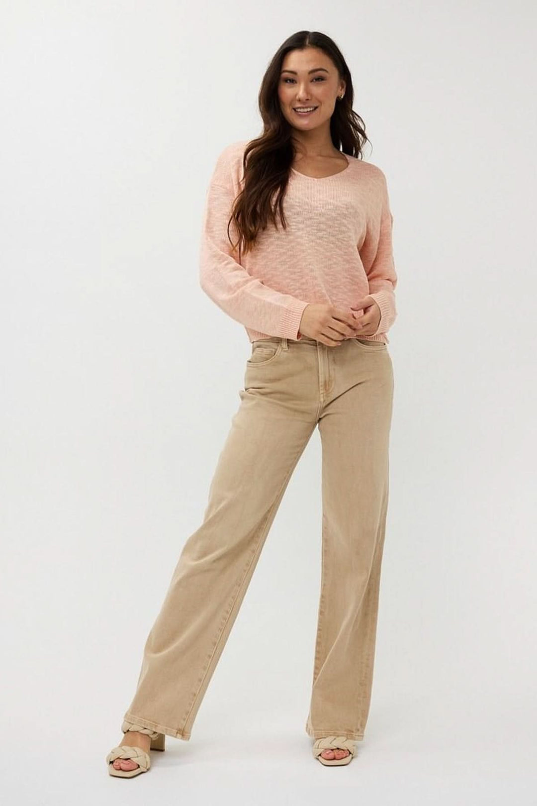 Chandail en tricot ajouré rose avec col en V, porté avec un pantalon beige, look décontracté et élégant.