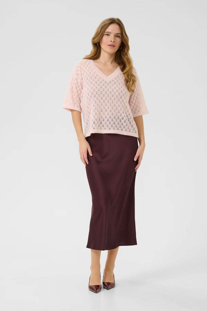 Femme portant un chandail en tricot ajouré rose et jupes marron, style décontracté et féminin.