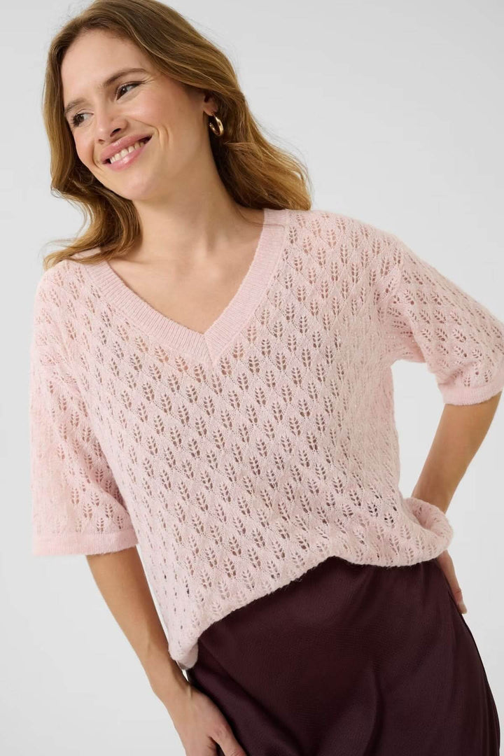 Femme portant un chandail en tricot ajouré rose à col en V, avec manches courtes et ourlet fluide.