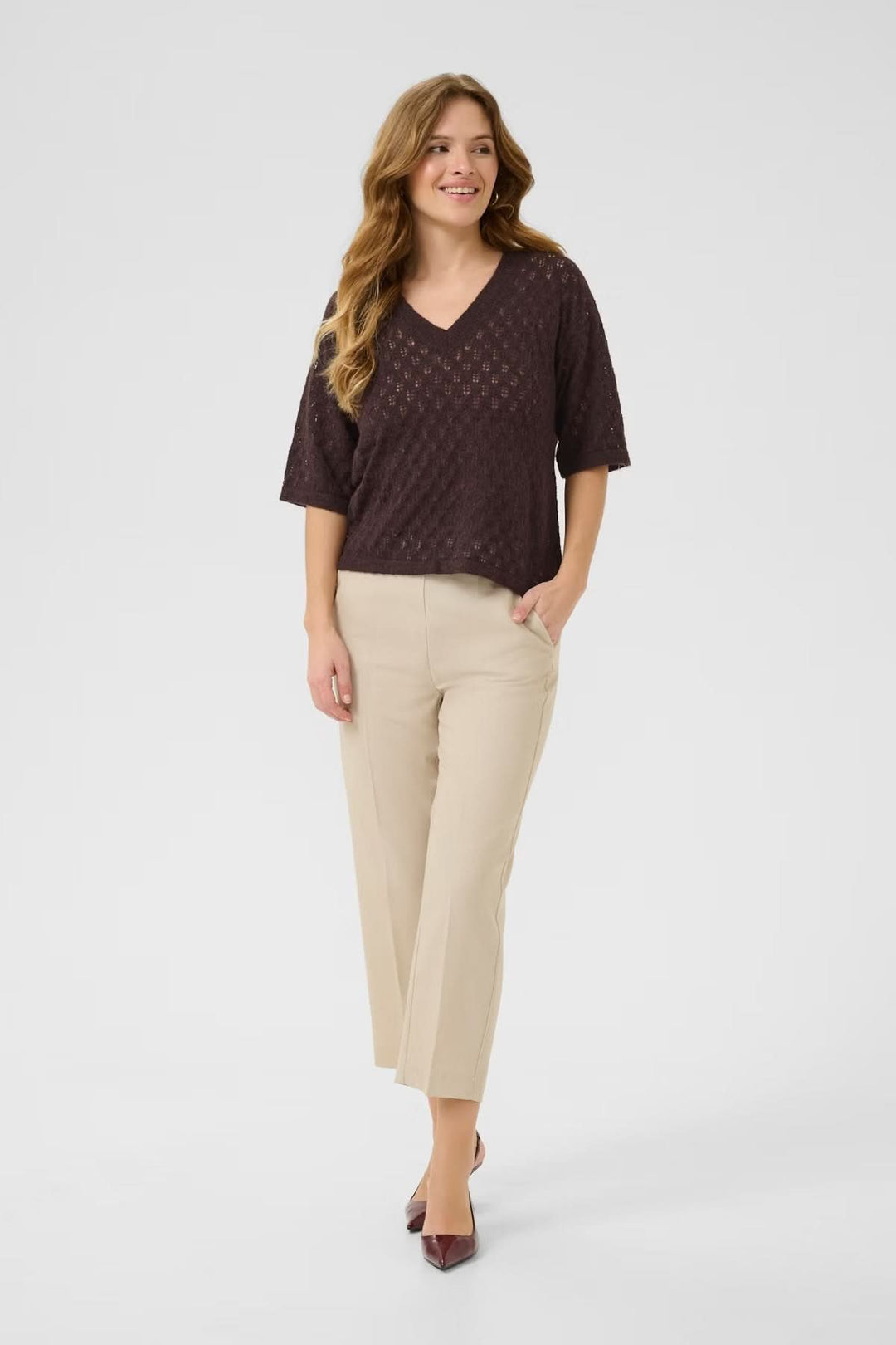 Chandail en tricot ajouré à col en V, léger et texturé, associé à un pantalon beige et des escarpins.