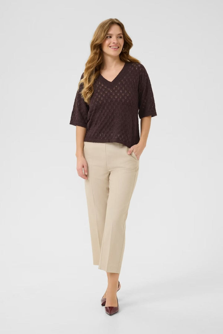 Chandail en tricot ajouré à col en V, léger et texturé, associé à un pantalon beige et des escarpins.