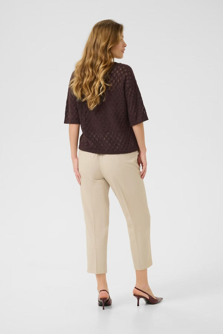 Femme de dos portant un chandail en tricot ajouré à col en V, associé à un pantalon beige.