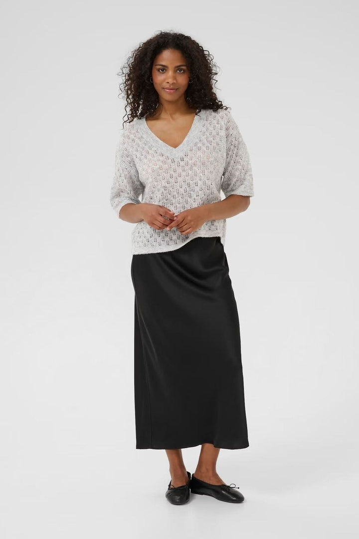 Femme portant un chandail en tricot ajouré à col en V, jupe longue noire, look décontracté et féminin.
