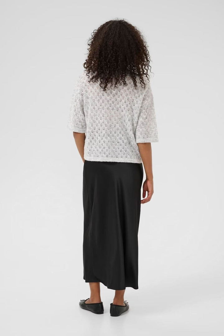 Vue arrière d'un chandail ajouré blanc à col en V et jupe longue noire, parfait pour un look décontracté.