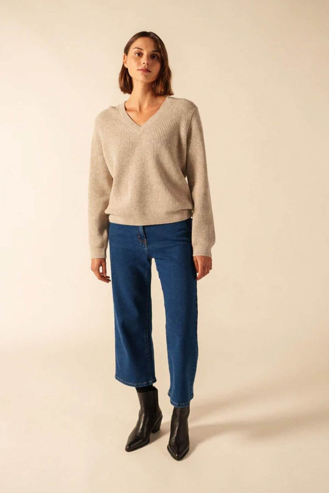 Femme portant un chandail en tricot à col en V avec jeans, décris moi le produit en français.