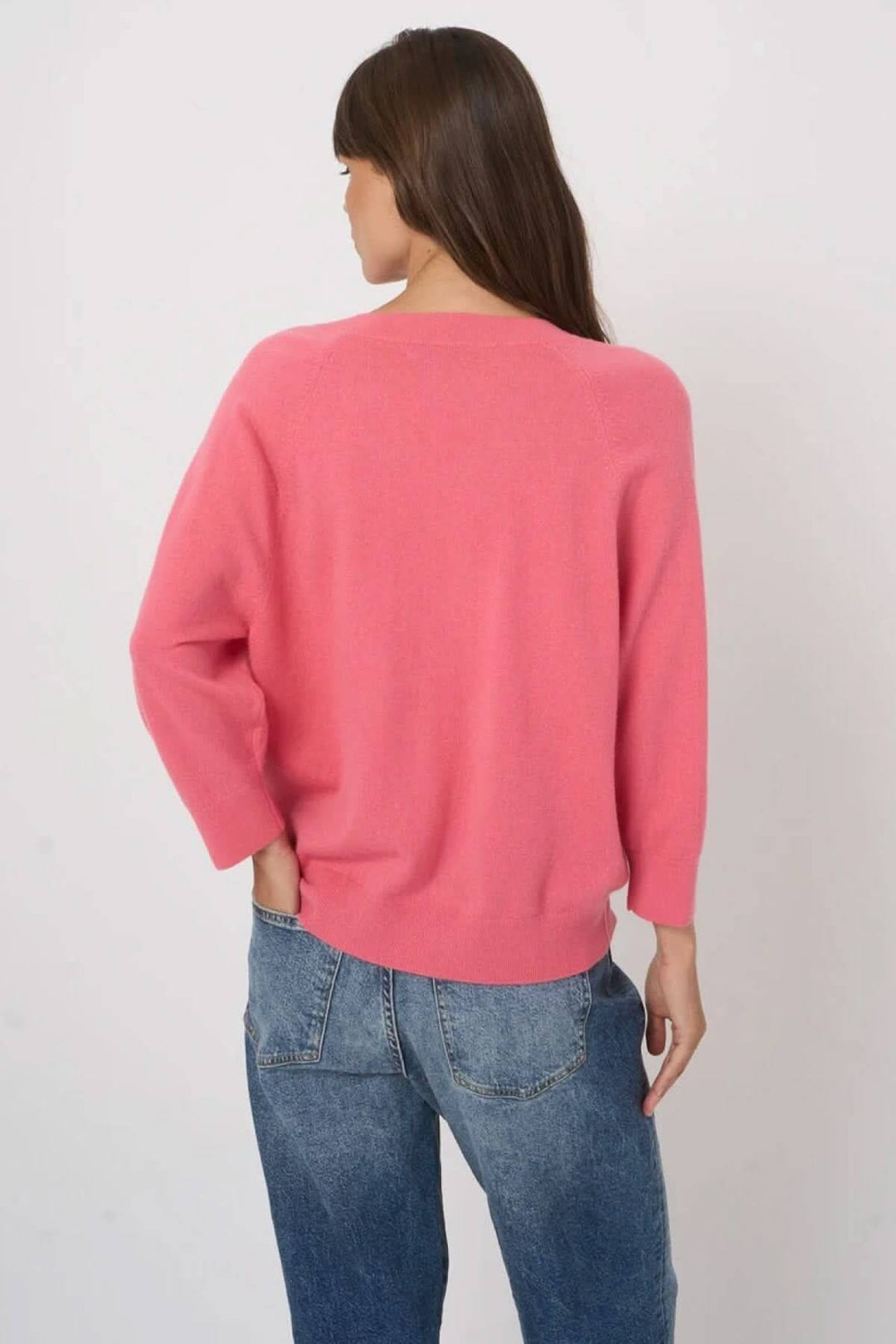 Femme portant un chandail en tricot à col en V, vue de dos, couleur rose, coupe droite et manches longues, avec jeans décontractés.
