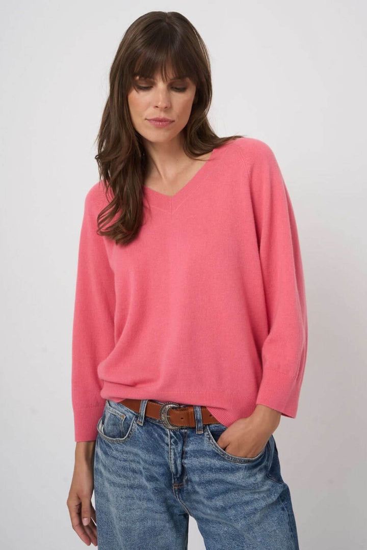 Chandail en tricot à col en V rose porté par une femme, style décontracté avec jeans, manches longues et coupe fluide élégante.