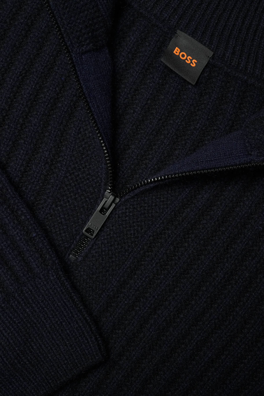 Detail of a ribbed knit, half-zip sweater with a dark color and a branded label. Chandail en tricot à demi-glissière.