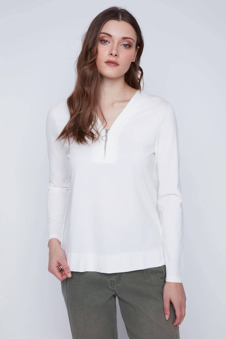 Femme portant un chandail encolure en V zippée blanc à manches longues, style décontracté, tissu extensible pour confort et liberté de mouvement.