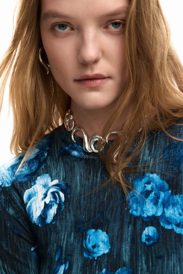 Femme portant un chandail fin à fleurs bleu avec manches longues pour une allure moderne et stylée.