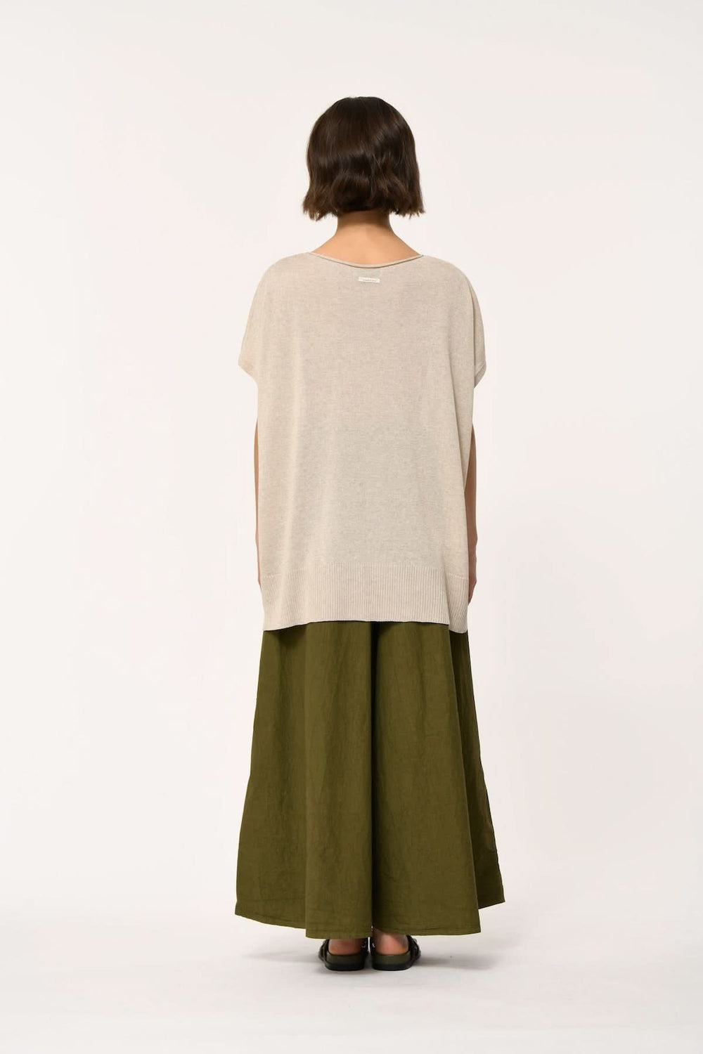 Femme portant un chandail fluide à manches courtes amples, de dos, associé à un pantalon large vert olive, style moderne décontracté.