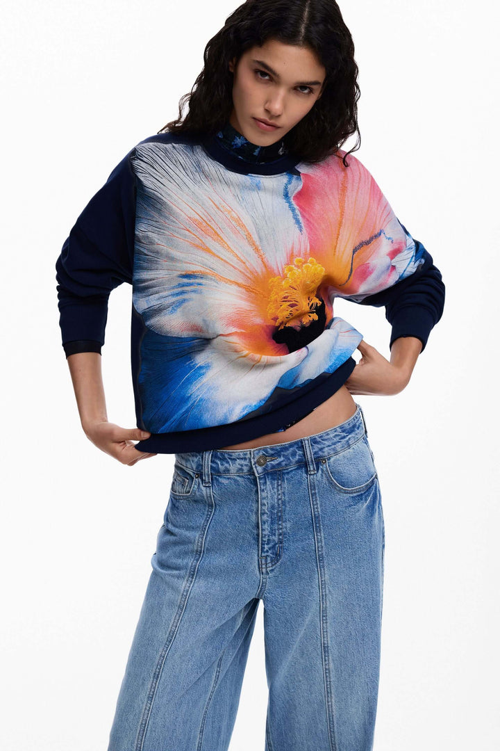 Chandail à grande fleur avec motif floral coloré, coupe confortable et style moderne, porté avec un jean. Décris moi le produit en français.