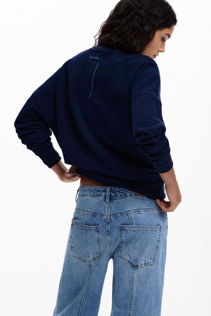 Femme portant un chandail à grande fleur bleu avec jean, vue de dos. Coordonné casual et tendance.