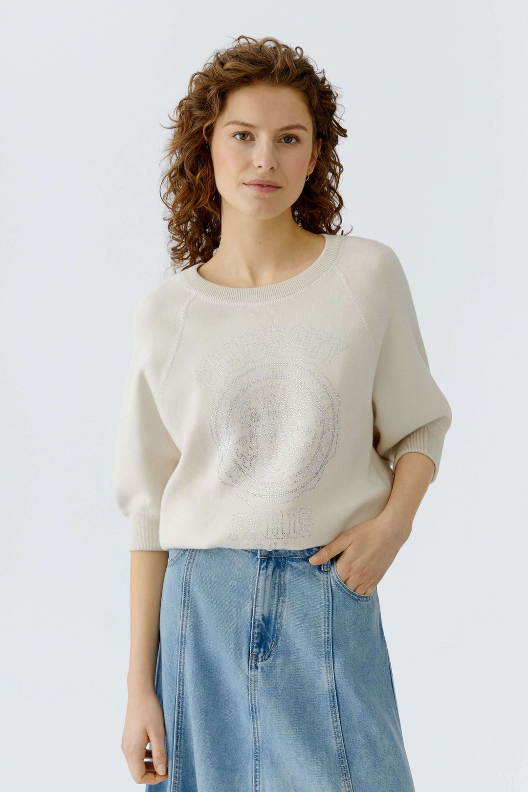 Femme portant un chandail à imprimé universitaire blanc avec manches trois-quarts, encolure ronde, sur jupe en jean.