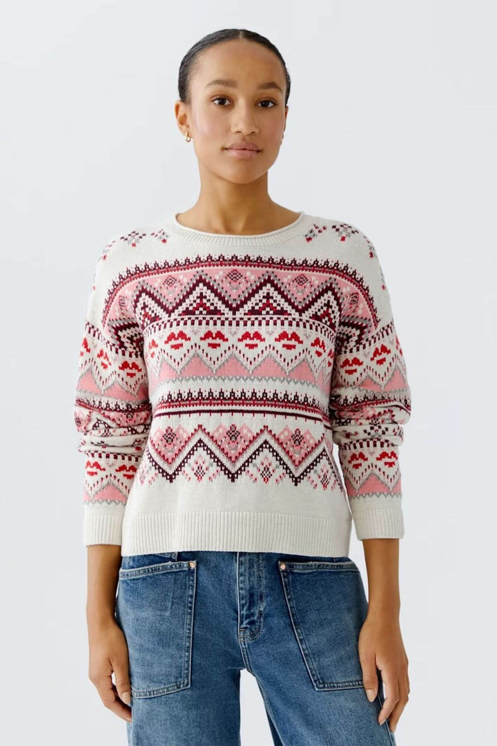 Chandail jacquard à motifs géométriques nordiques sur fond blanc, manches longues, porté avec un jean pour un look hivernal décontracté.