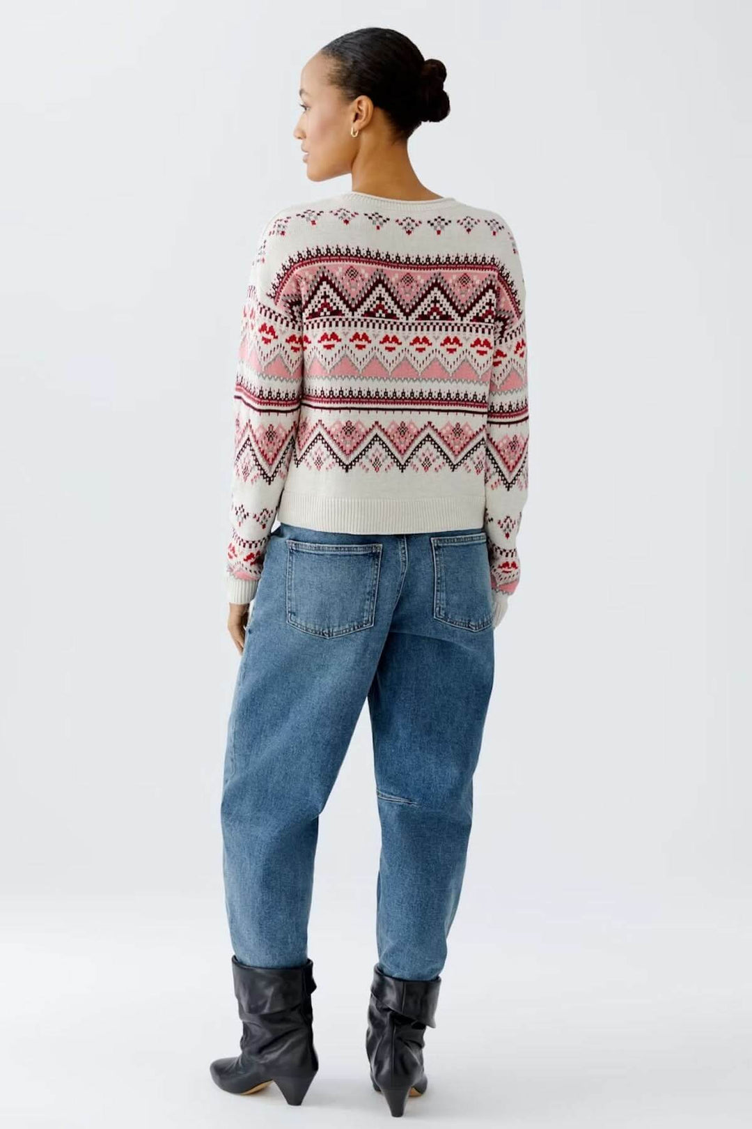 Personne portant un chandail jacquard à motifs géométriques nordiques, encolure ronde, avec un jean et bottes, vue de dos.