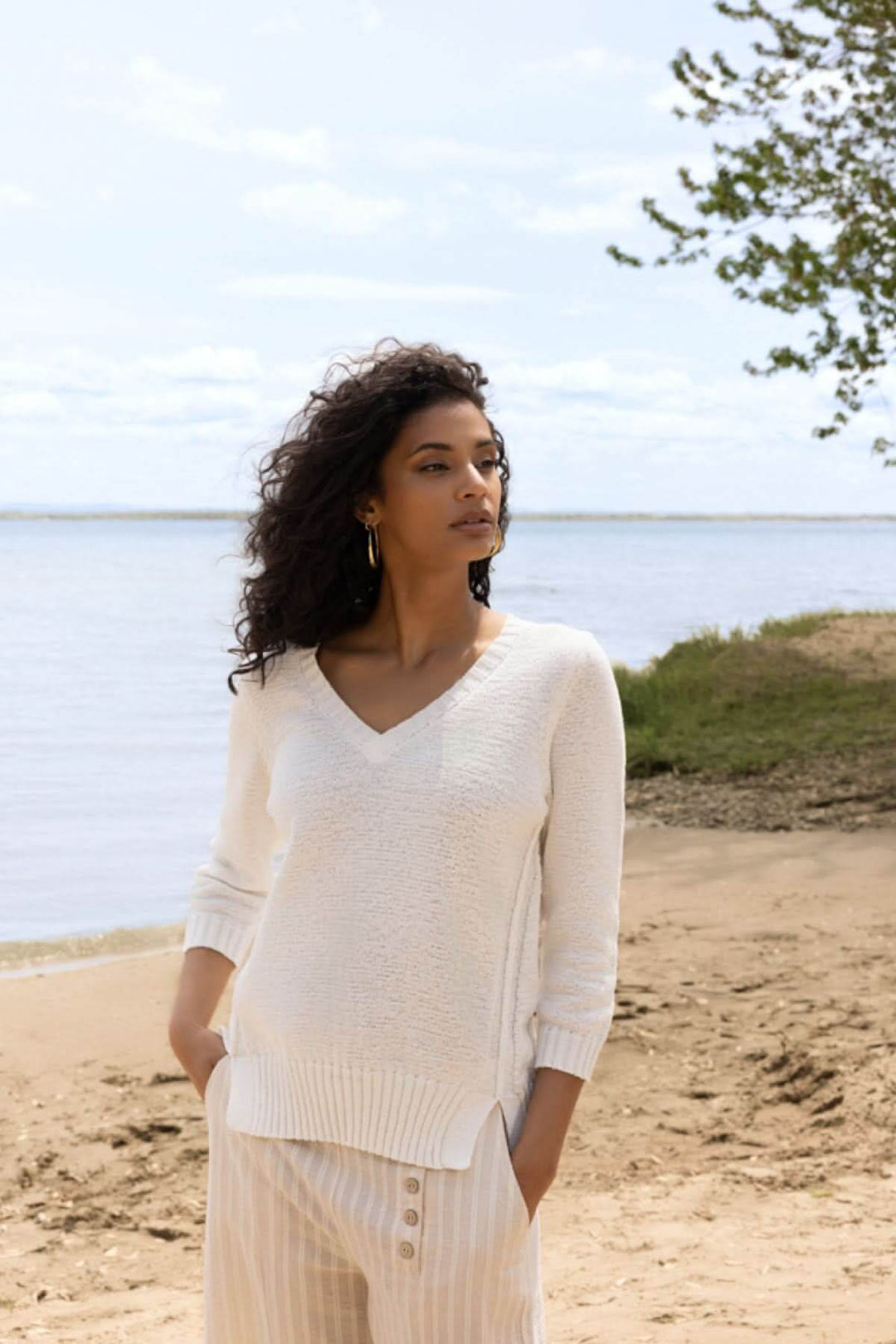 Femme portant un chandail léger col en V texturé sur une plage ensoleillée.