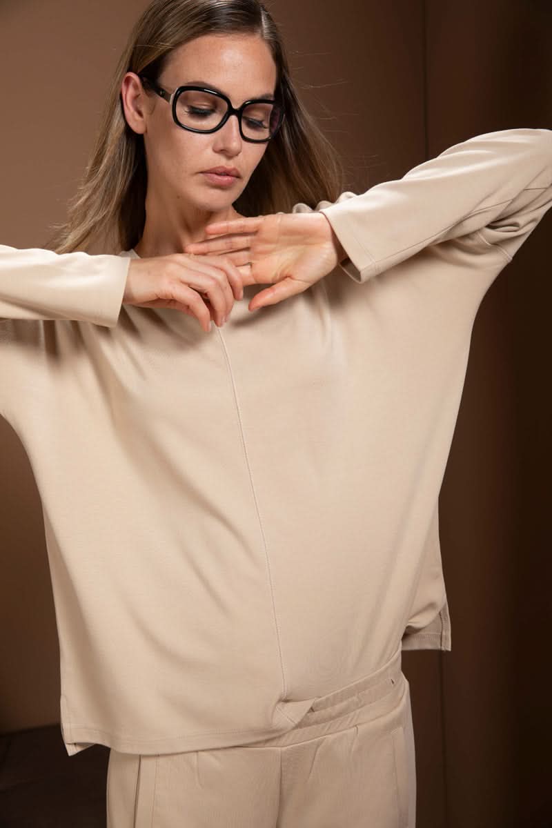 Chandail minimaliste avec coupe fluide, encolure en V et manches longues, porté par une femme pour un look moderne et décontracté.