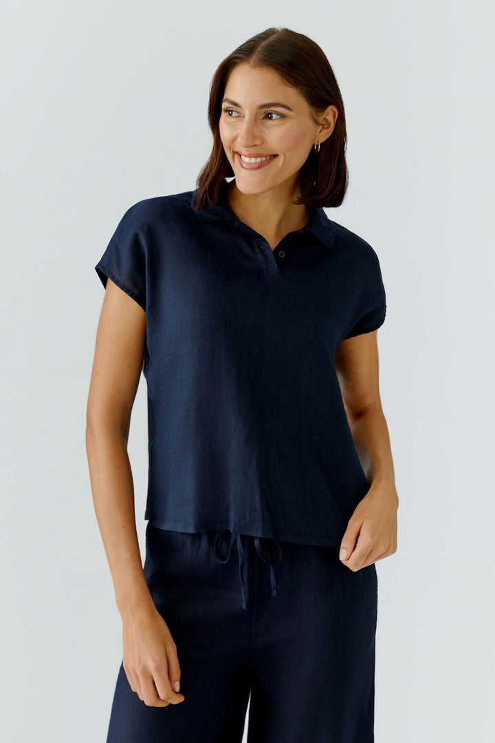 Femme portant un chandail polo fluide à manches courtes bleu foncé, style moderne et épuré, pour un look minimaliste et confortable.