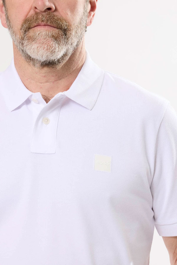 Homme portant un polo blanc à logo BOSS ton sur ton, col polo et finitions élégantes.