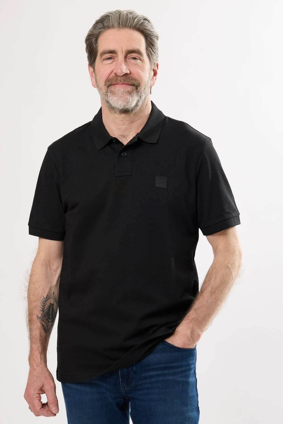 Homme souriant portant un polo noir à détails ton sur ton et manches courtes, parfait pour un look décontracté.