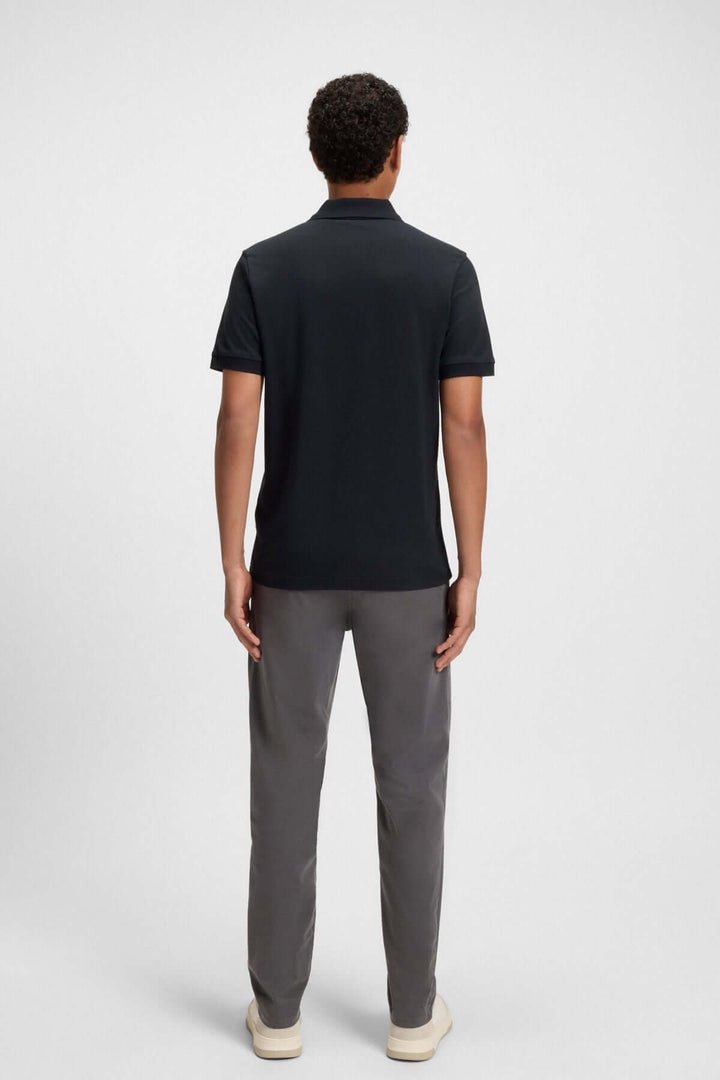 Homme portant un polo noir Boss avec pantalon gris, vu de dos, illustrant un style casual-chic.