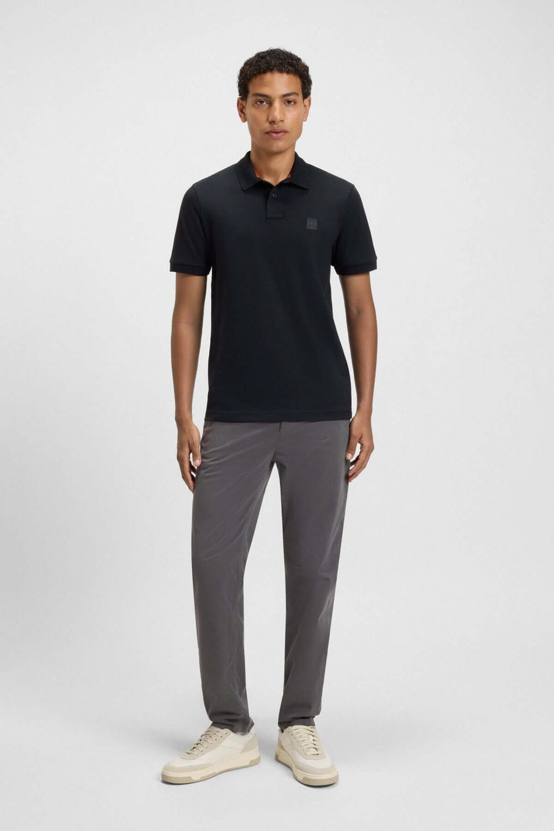 Homme en polo noir à logo Boss, pantalon gris, style décontracté et chic.
