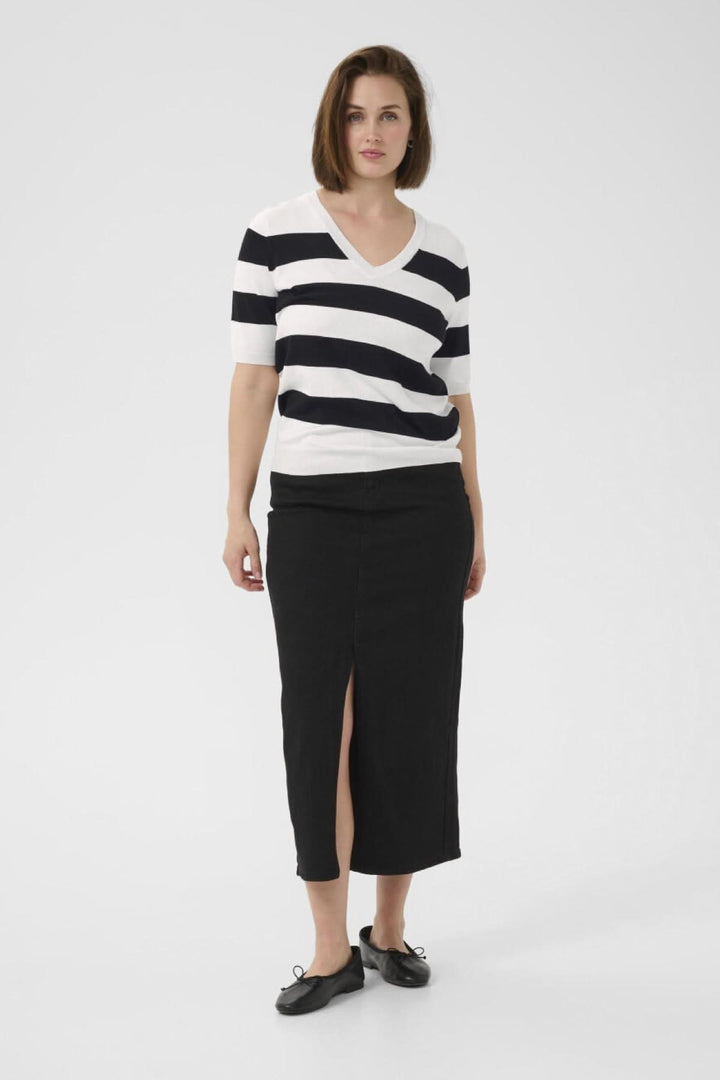 Chandail rayé à col en V, confortable et moderne, associé à une jupe noire fendue pour un look décontracté élégant.