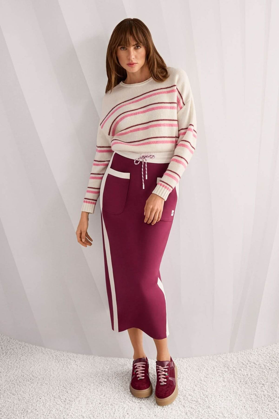 Femme portant un chandail rayé en maille douce avec une jupe bordeaux, élégance moderne et confortable.