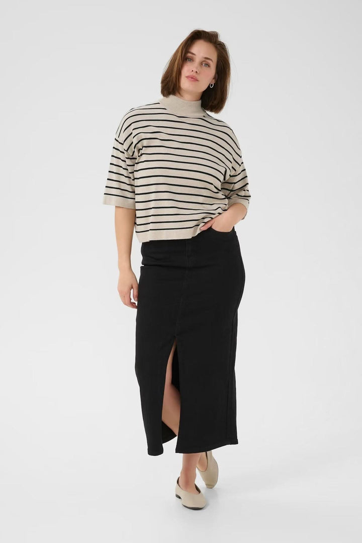 Femme portant un chandail à rayures fines et col montant avec une jupe longue noire et des chaussures claires.