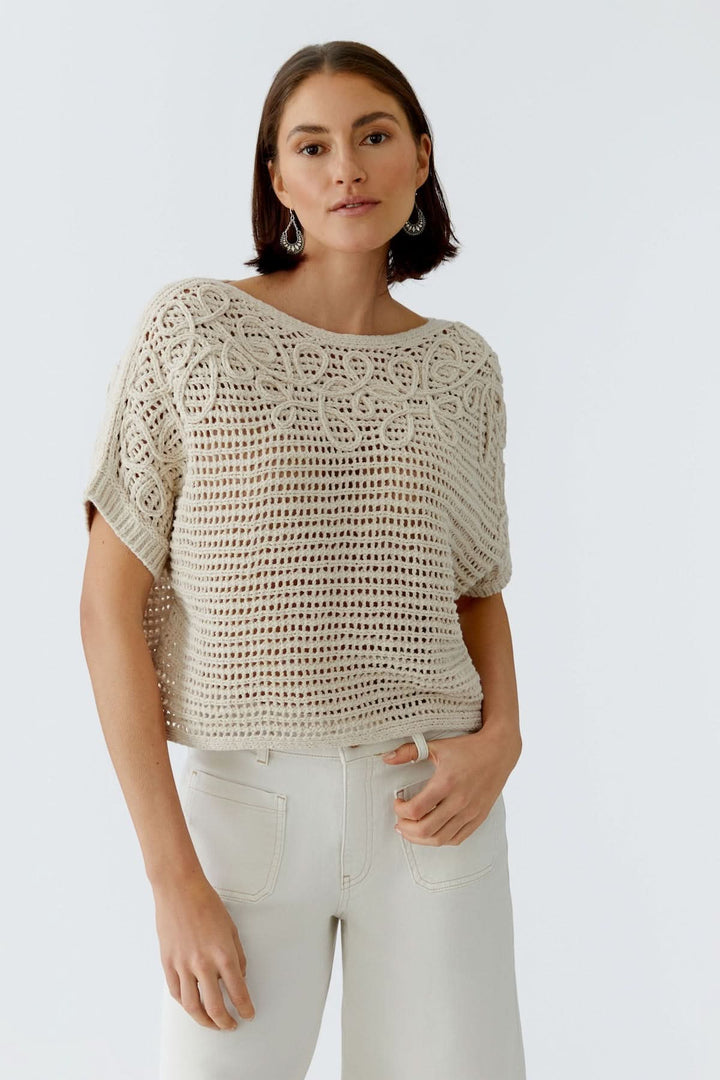 Femme portant un chandail tricot ajouré texturé beige élégant avec encolure dégagée. Décris moi le produit en français.