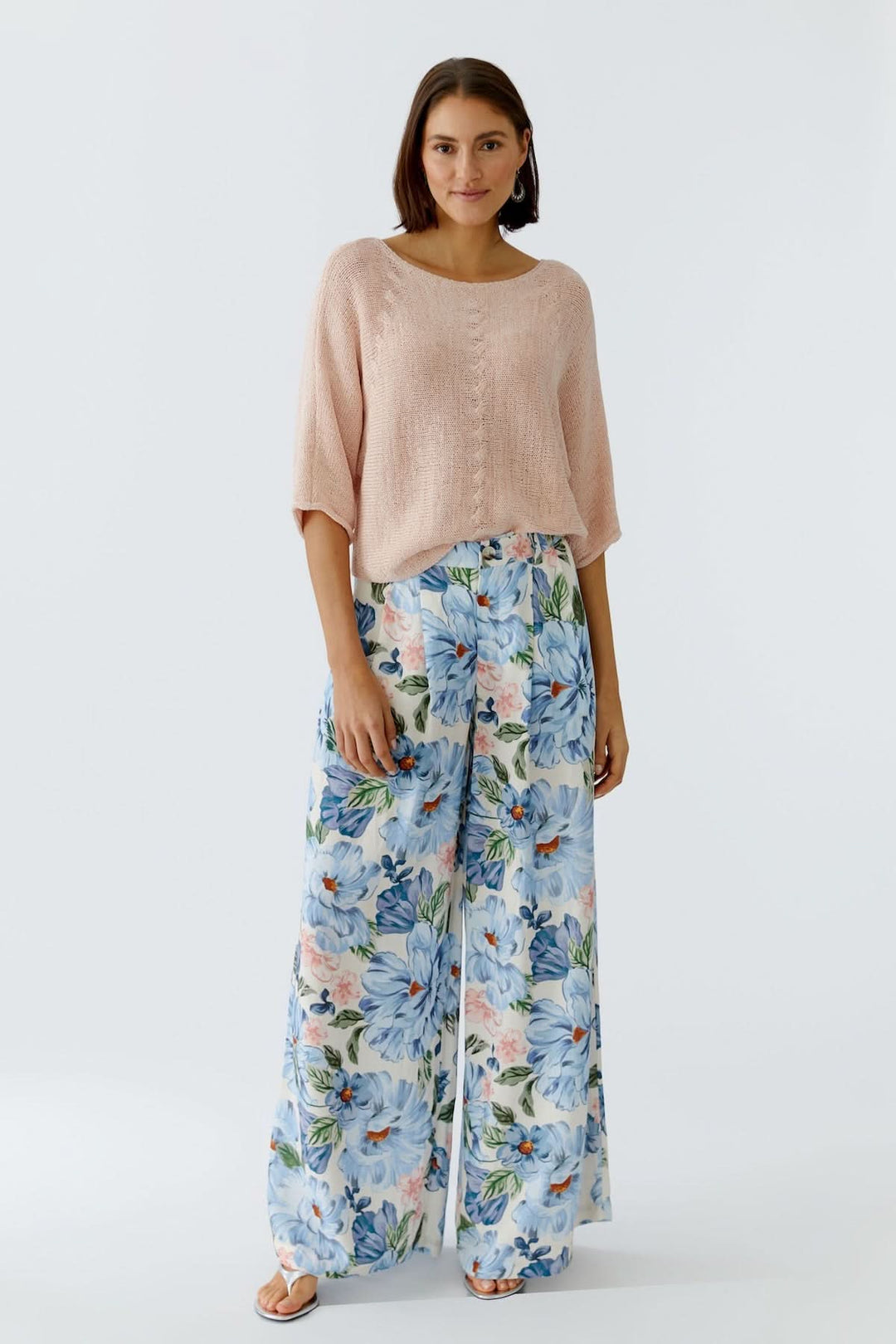 Femme portant un chandail tricot léger et pantalon à motifs floraux, offrant une silhouette décontractée et moderne.