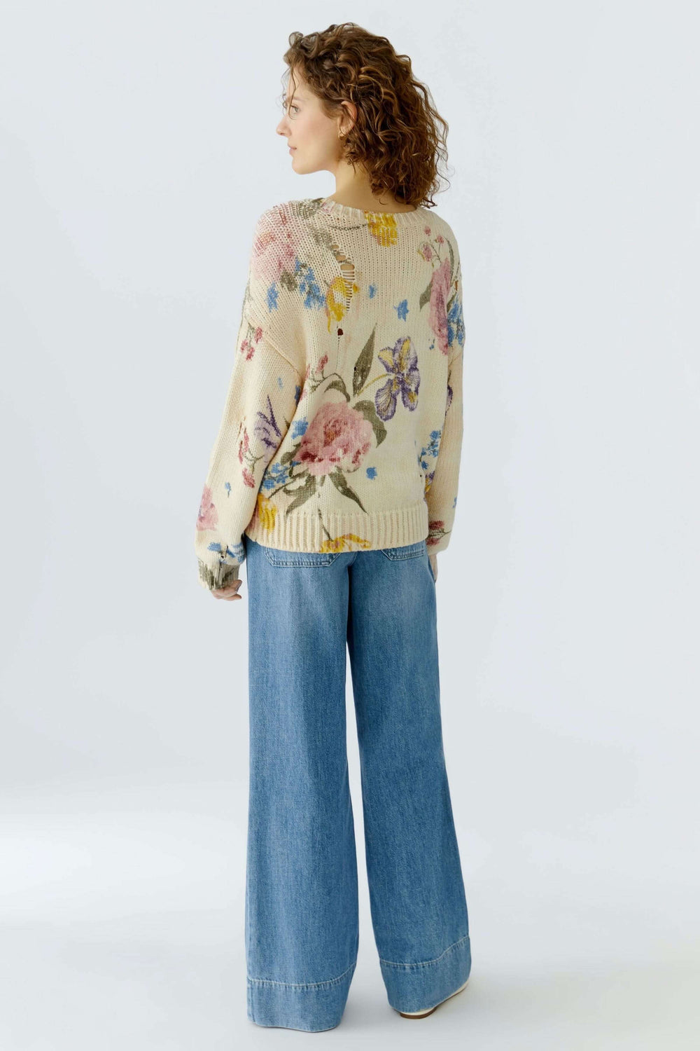 Femme portant un chandail vintage tendance avec imprimé floral artistique et design ajouré, associée à un jean large.