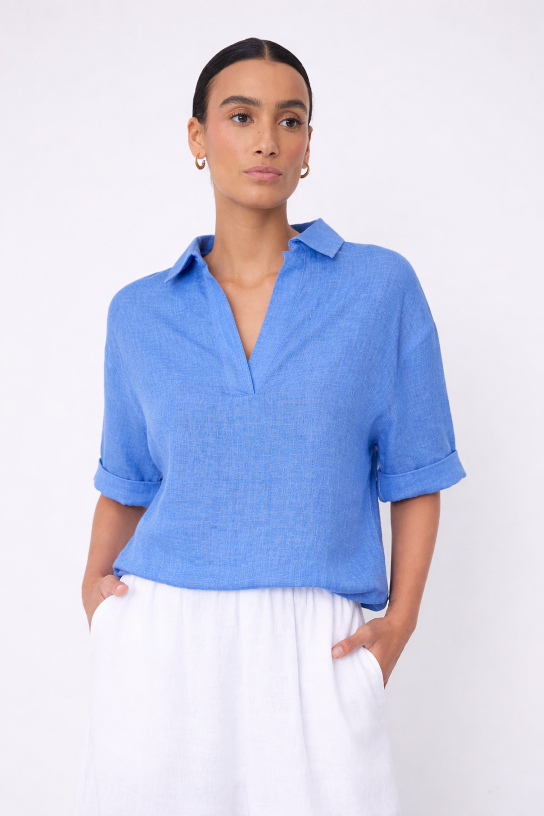 Femme portant une blouse courte en lin à col ouvert bleue avec manches courtes retroussées, style décontracté pour la saison chaude.
