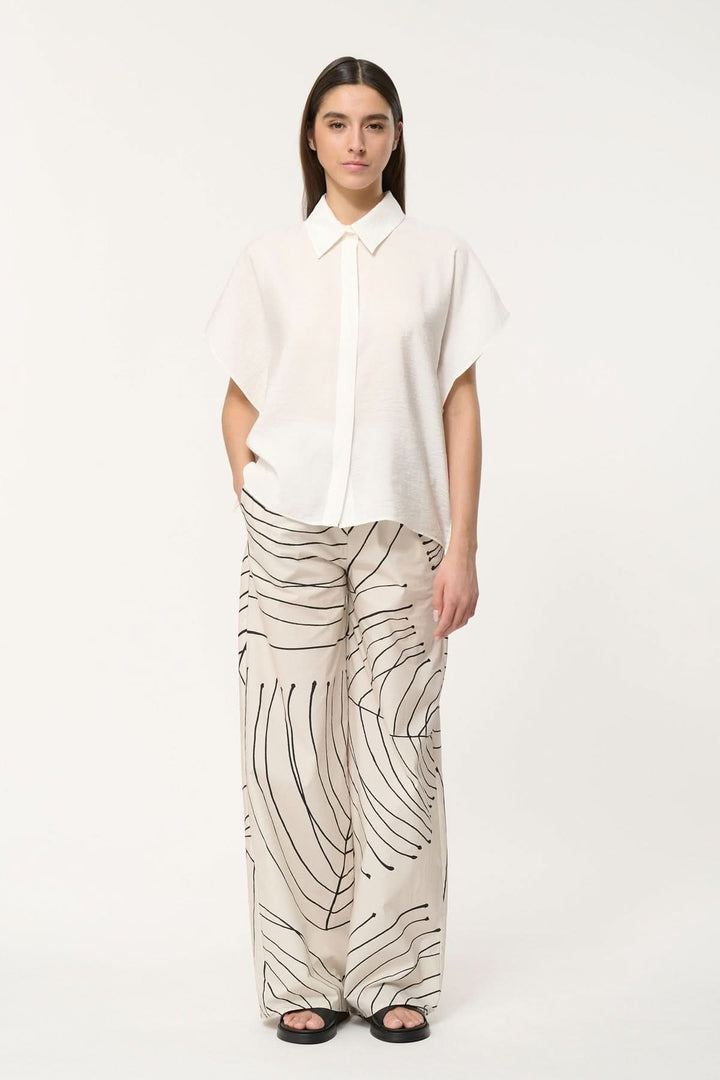 Femme portant une chemise légère à coupe ample et un pantalon à motifs modernes, style décontracté.