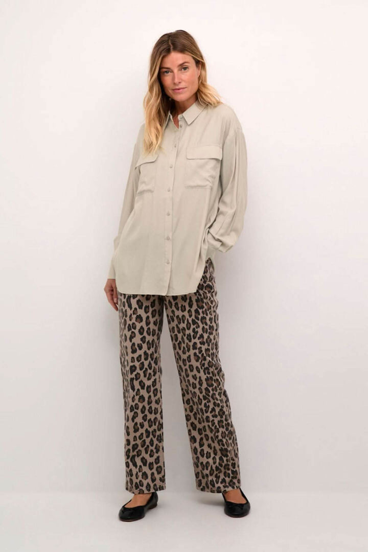 Chemise moderne beige avec poches, manches amples, pantalon léopard, look décontracté et soigné.
