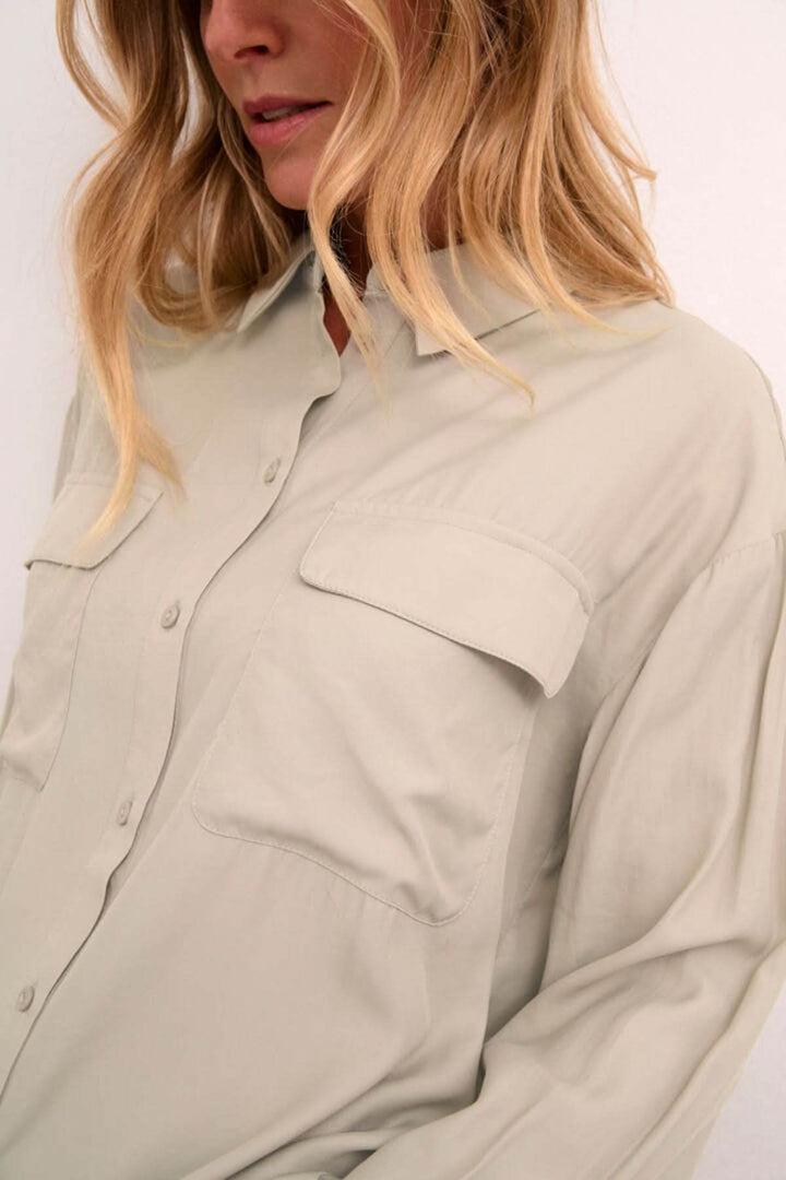 Chemise moderne beige avec poches plaquées, manches amples et col classique, style décontracté et soigné.