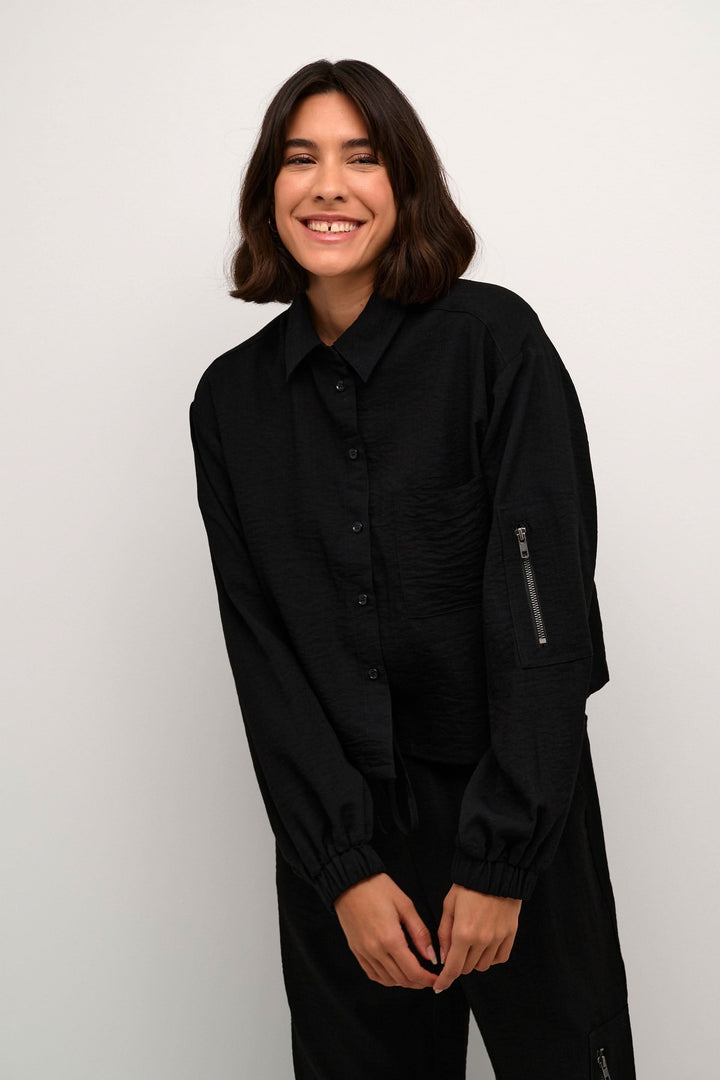 Femme souriante portant une chemise Elenor noire à manches longues et fermeture éclair sur une manche.