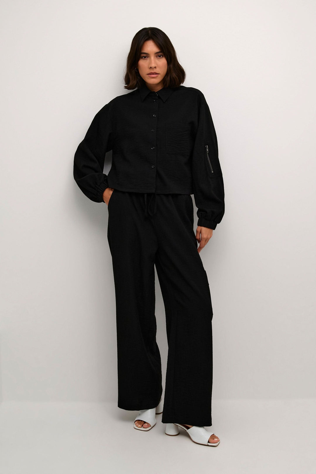 Chemise Elenor à manches longues avec boutons, style décontracté et élégant, portée avec un pantalon noir.