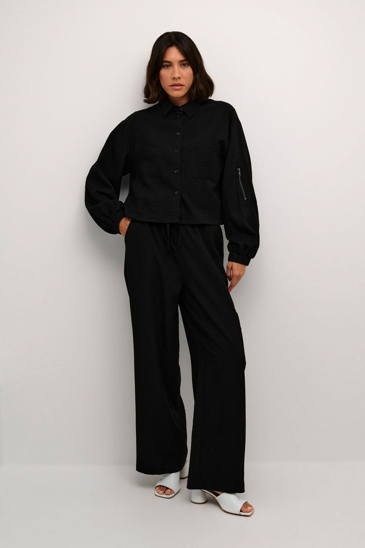Chemise Elenor à manches longues avec boutons, style décontracté et élégant, portée avec un pantalon noir.