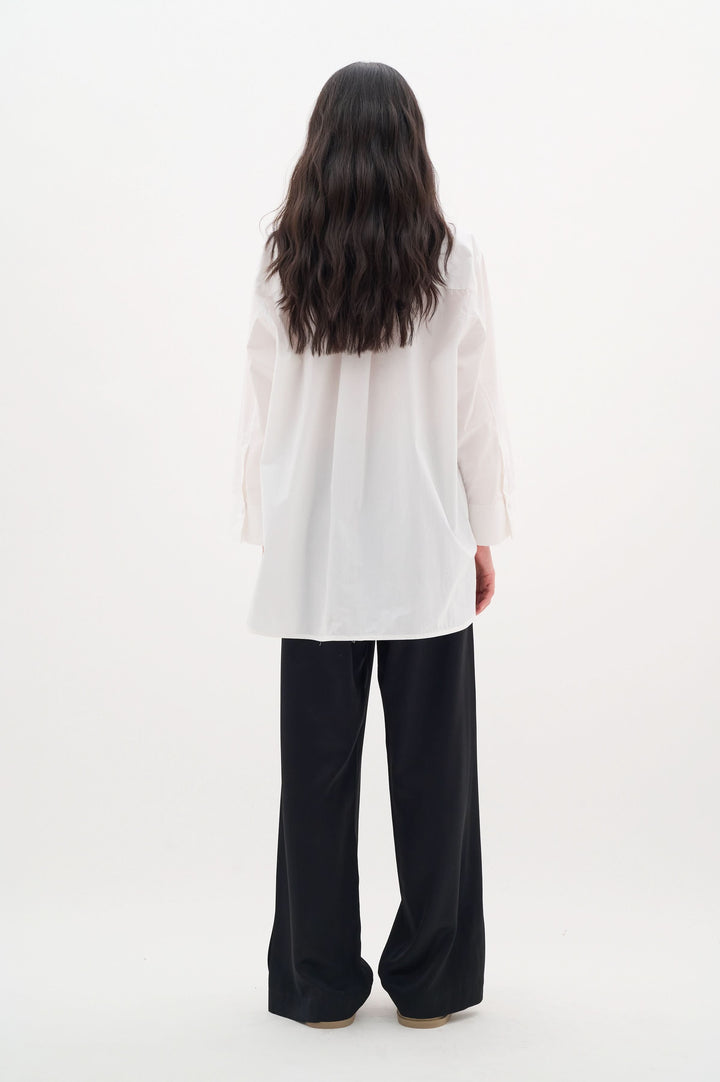 Chemise Merlissa oversize blanche à l'arrière, style chic minimaliste avec pantalon noir.