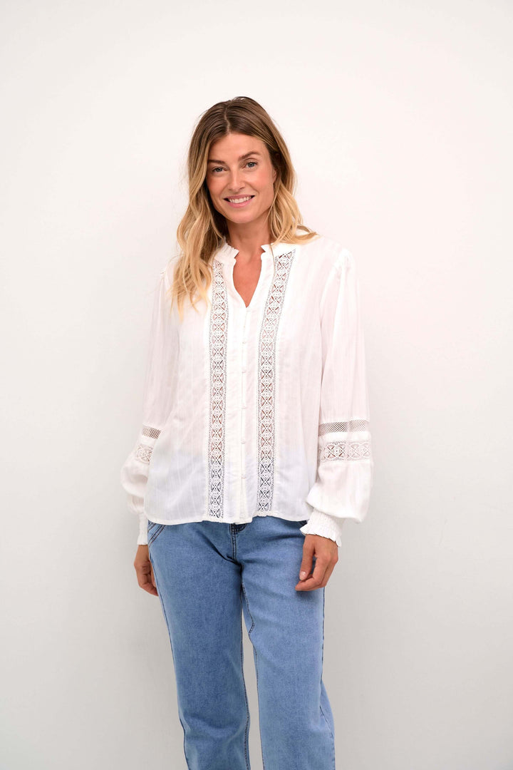 Chemise Paula romantique en blanc avec dentelle, manches bouffantes et patte de boutonnage, portée avec un jean.