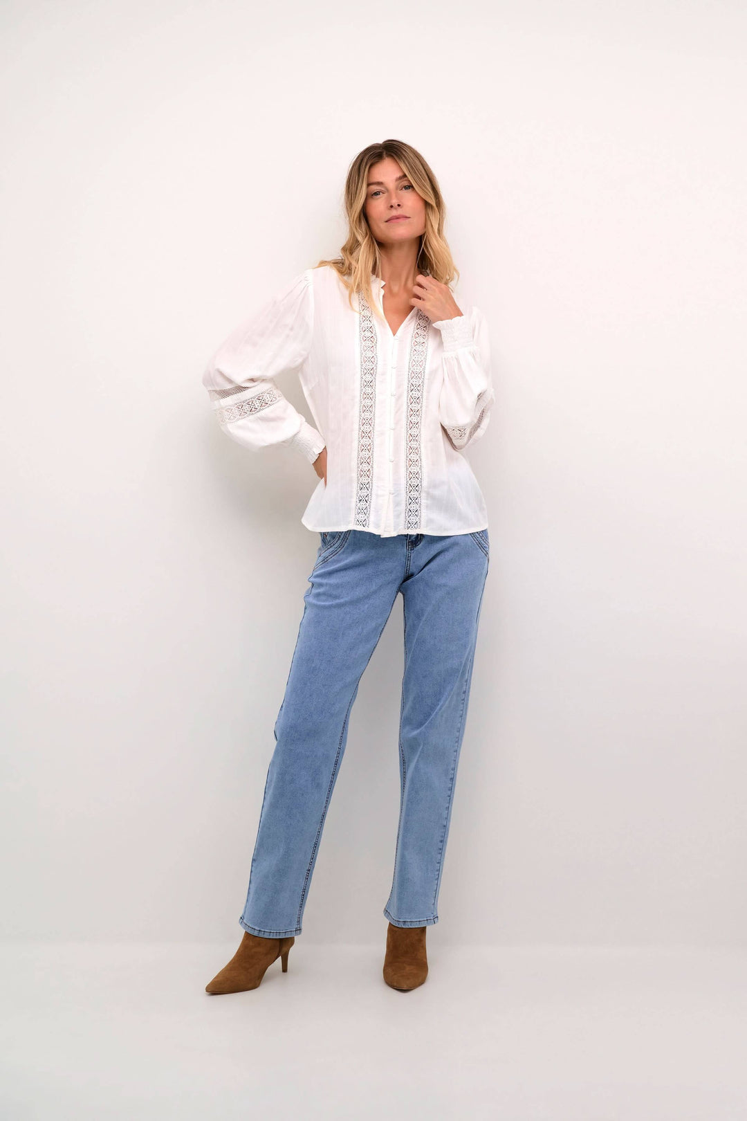 Femme en chemise blanche à dentelle, jean clair et bottines, look romantique et élégant.