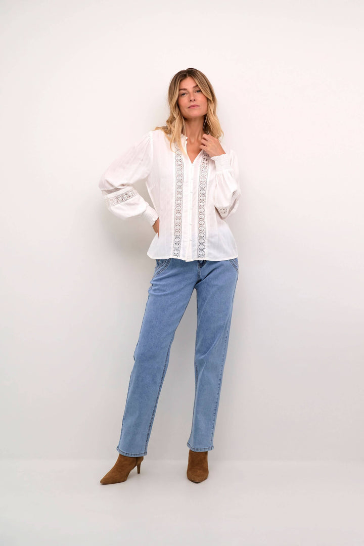 Femme en chemise blanche à dentelle, jean clair et bottines, look romantique et élégant.