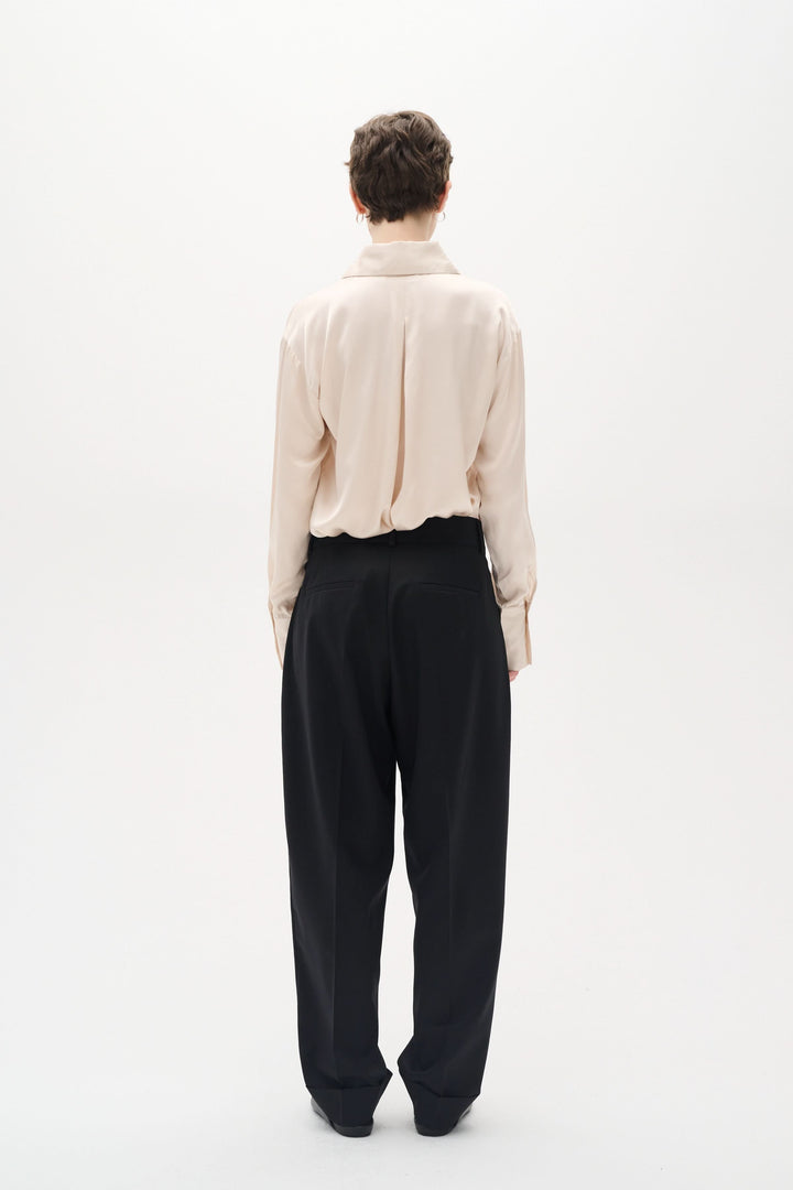Vue arrière de la chemise satinée Pauline, avec coupe ample et manches longues, portée avec un pantalon noir.
