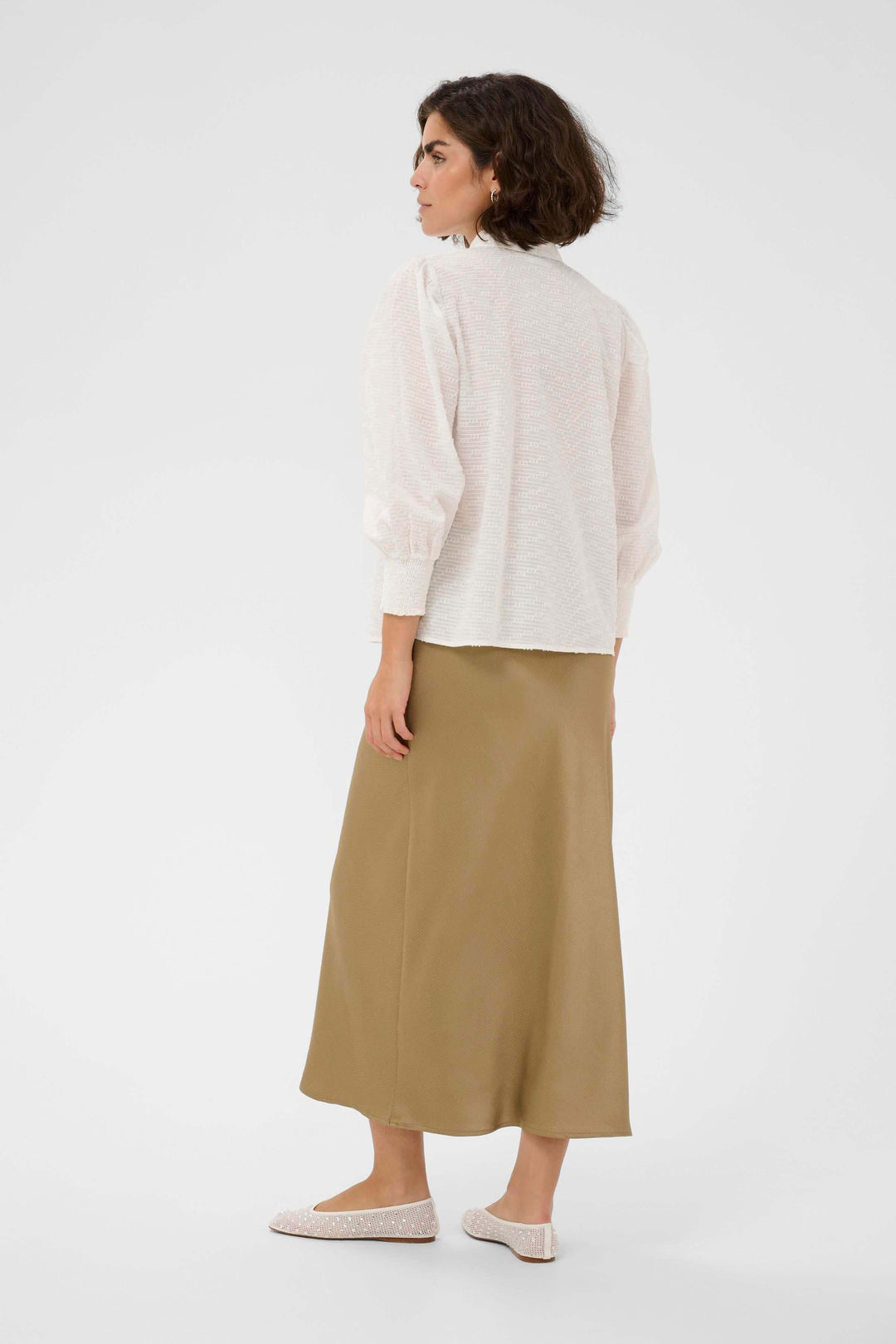 Femme portant la Chemise Penelope texturée à manches bouffantes, vue de dos, avec jupe et mocassins.