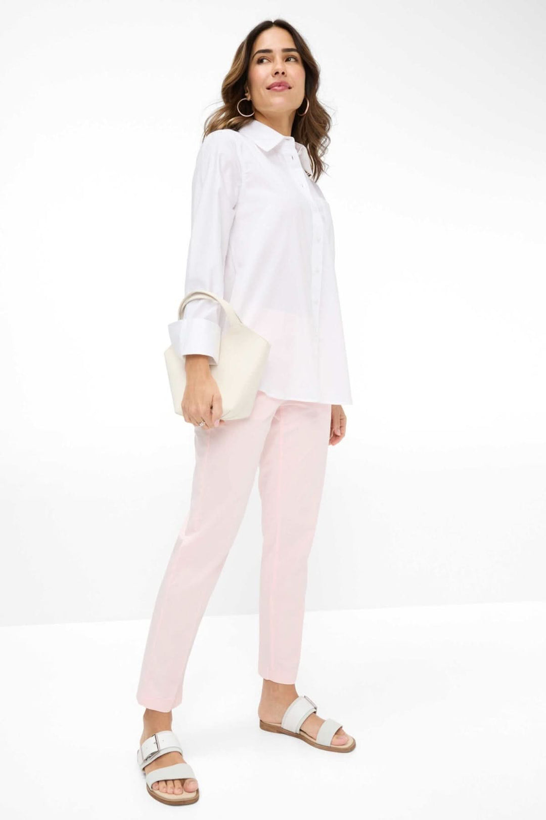 Femme portant le chemisier Viki en blanc avec un pantalon rose, accessoire moderne et chic.