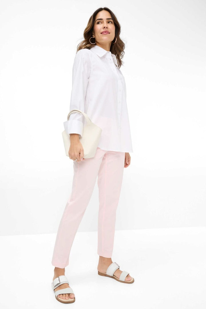 Femme portant le chemisier Viki en blanc avec un pantalon rose, accessoire moderne et chic.